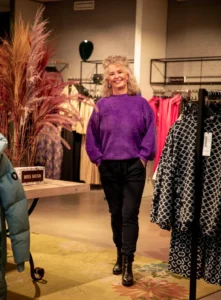 Herma imago-stylist met zelfverzekerde uitstraling tussen kledingrekken